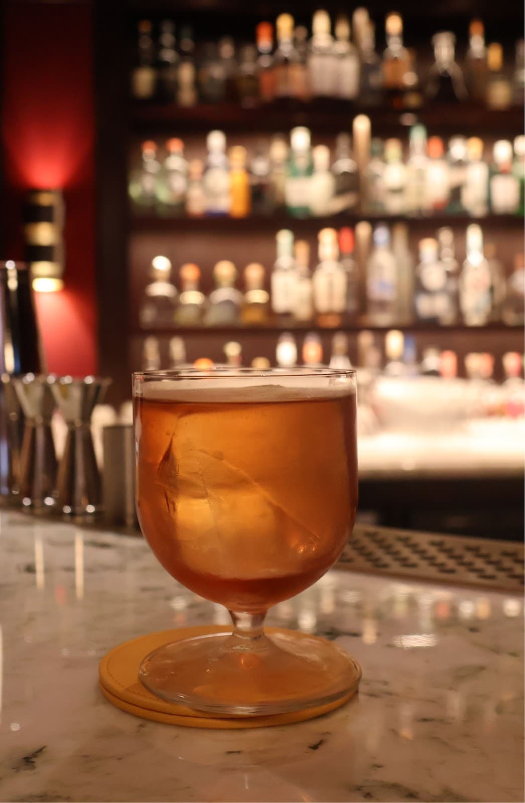 Close-up of a cocktail glass on a marble bar with bottles blurred in the background in London