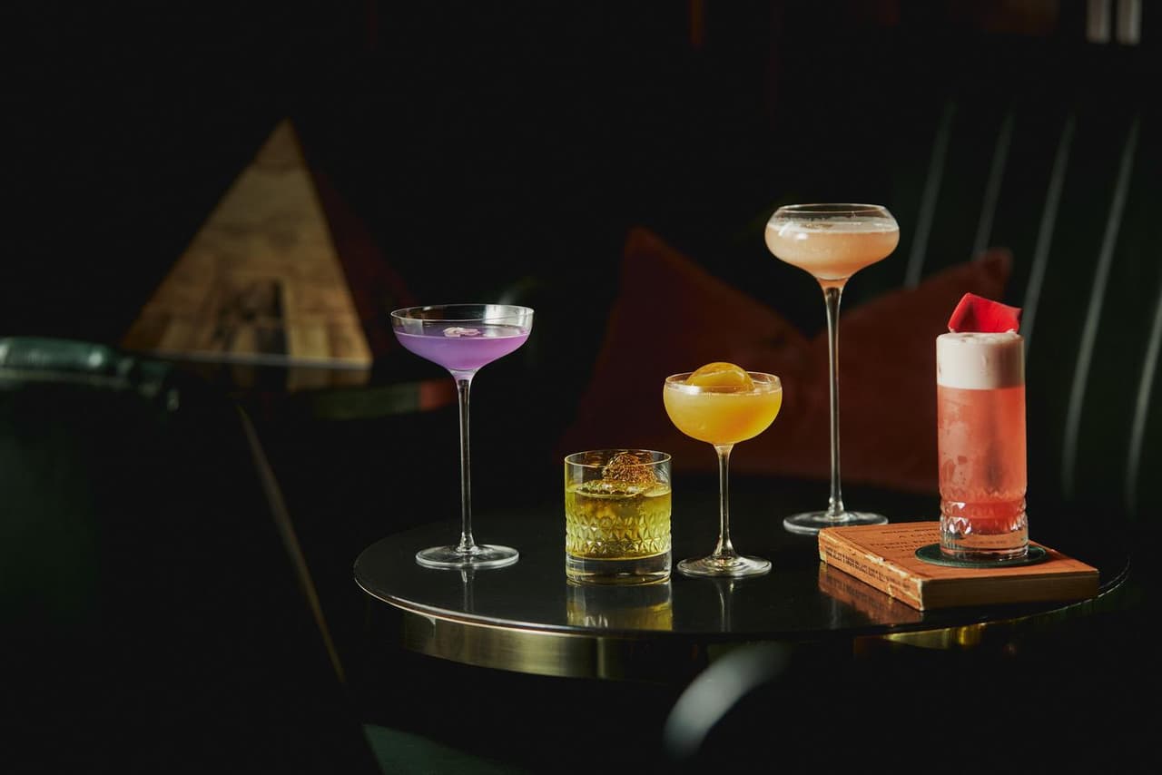 Assorted cocktails on a dark round table in a dimly lit bar in London