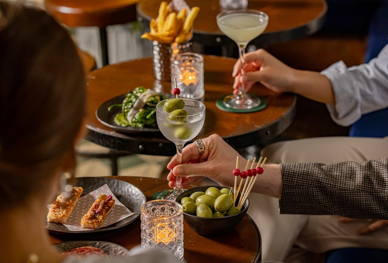 Hands holding cocktails with olives in a cozy bar setting in London