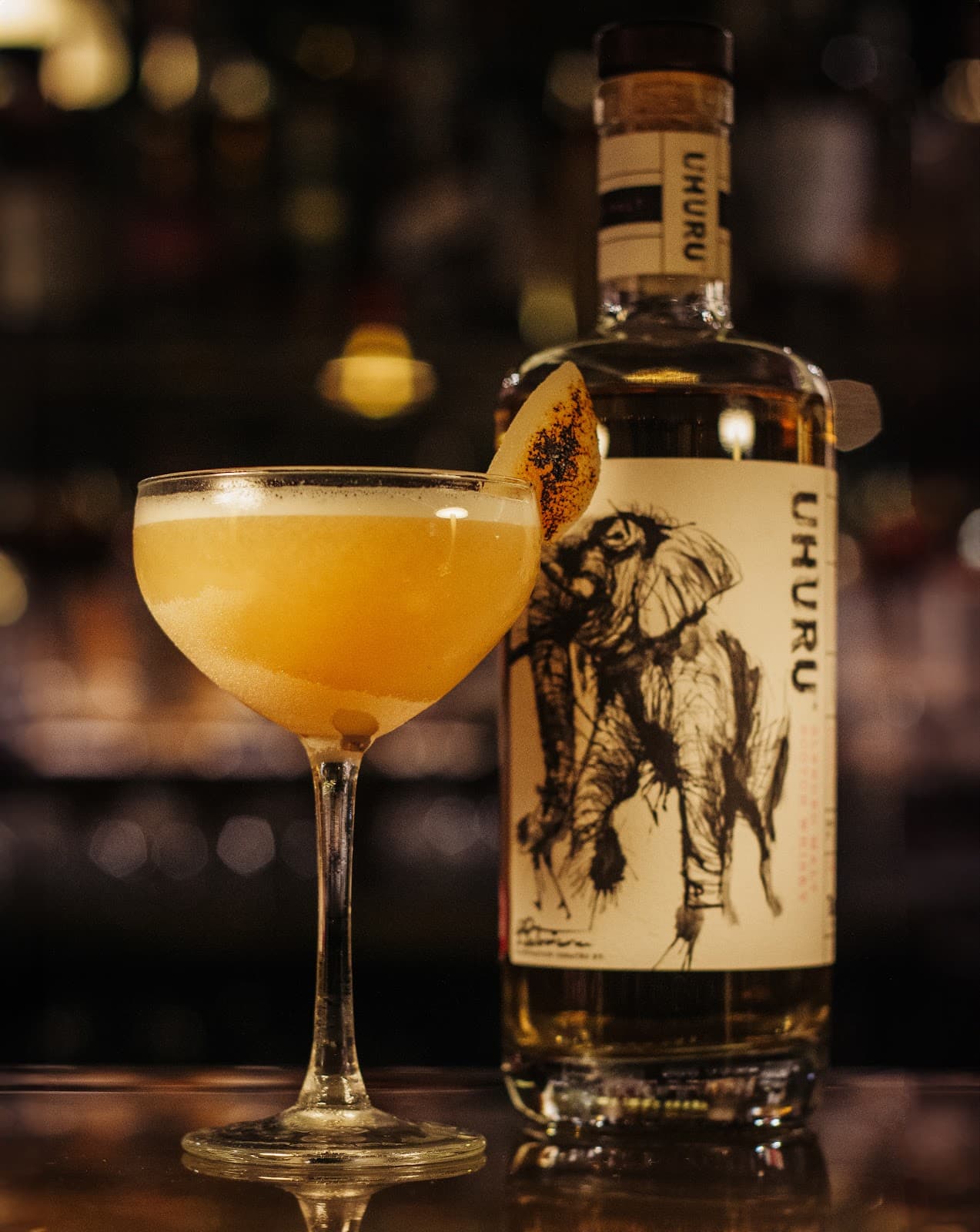 Cocktail glass with garnish in front of Uhuru bottle on bar counter in Edinburgh