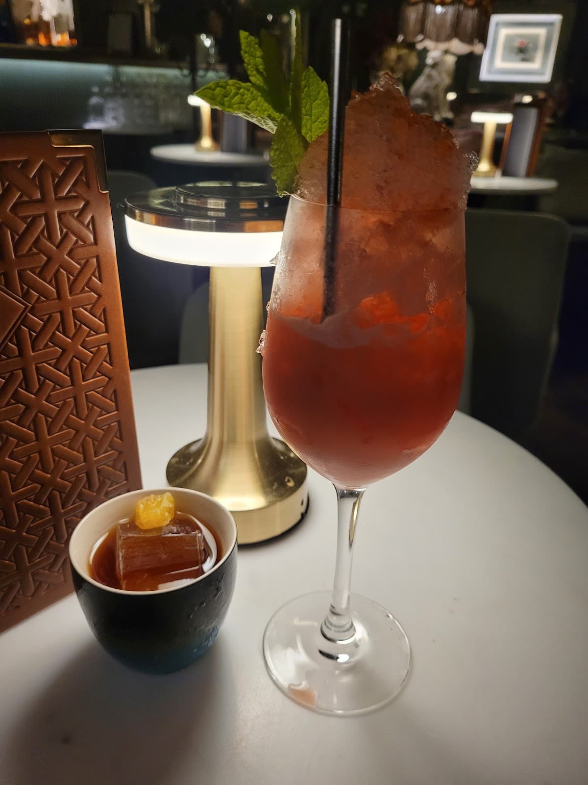 Close-up of red cocktail with mint and ice on white table near warm lighting in Edinburgh