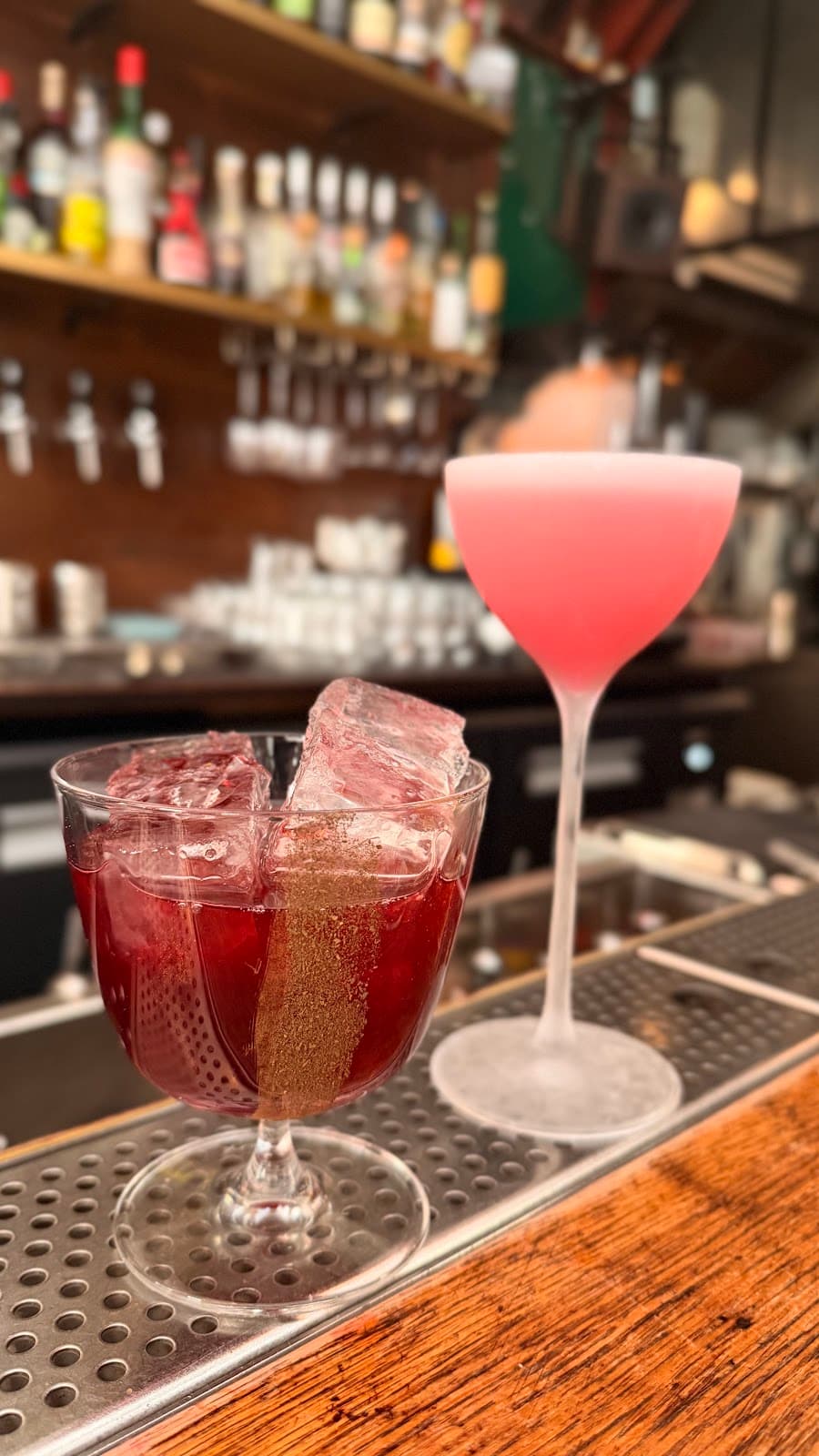 Two cocktails on a bar counter with bottles in the background in Paris