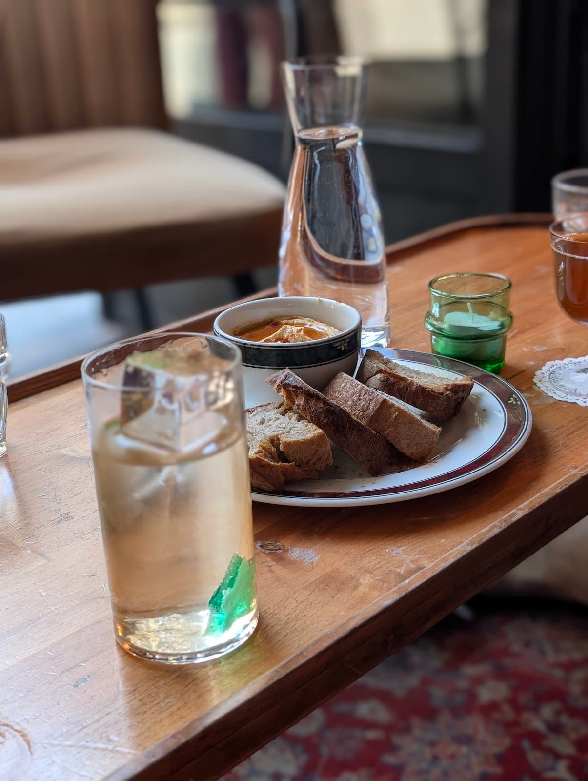 Table with cocktail glass, bread, and water carafe in a cozy setting in Paris
