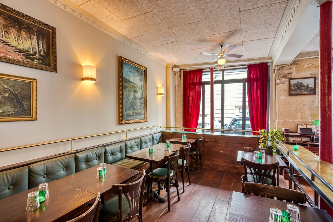 Bright interior with green upholstered seating and red curtains in a cocktail bar.