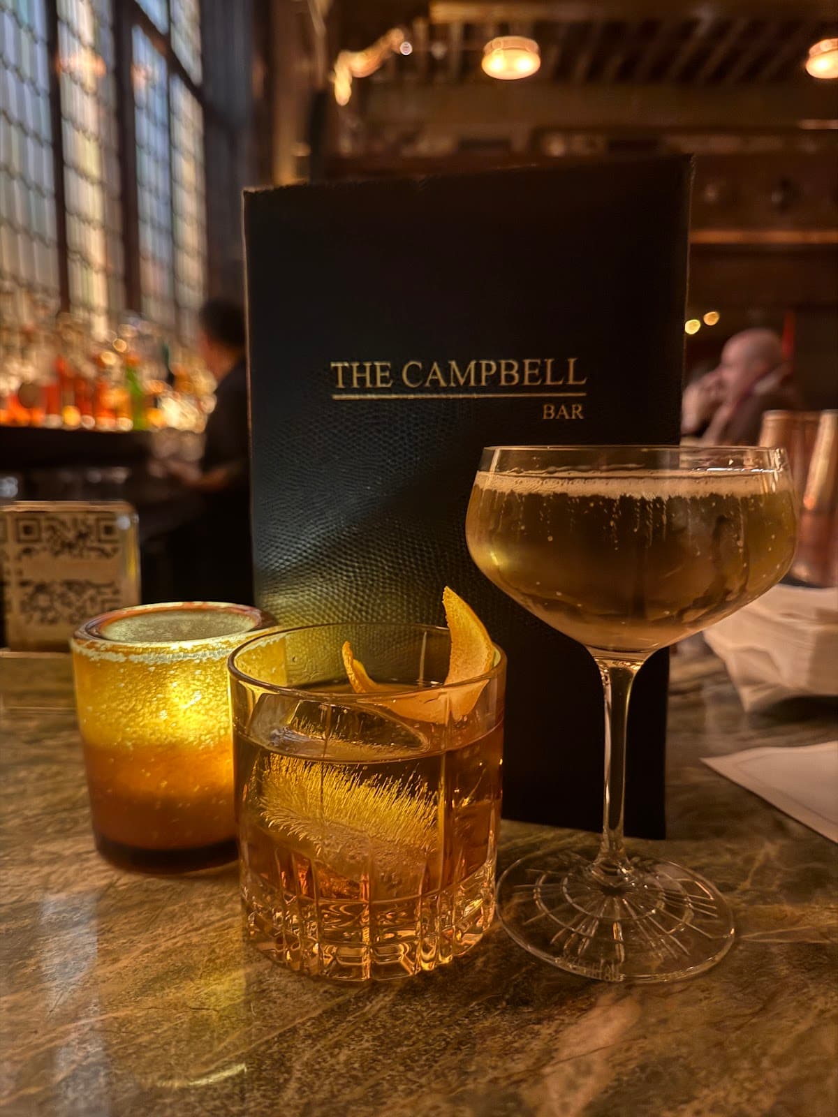 Cocktails on a marble bar next to a menu at The Campbell Bar in New York