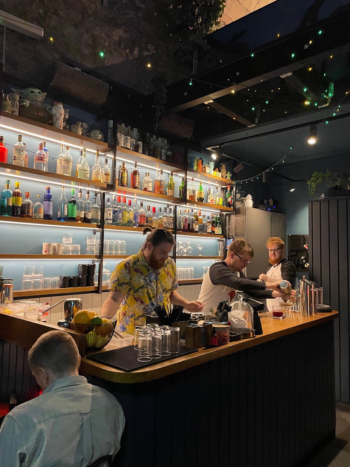 Three bartenders working at a well-lit bar with shelves of bottles