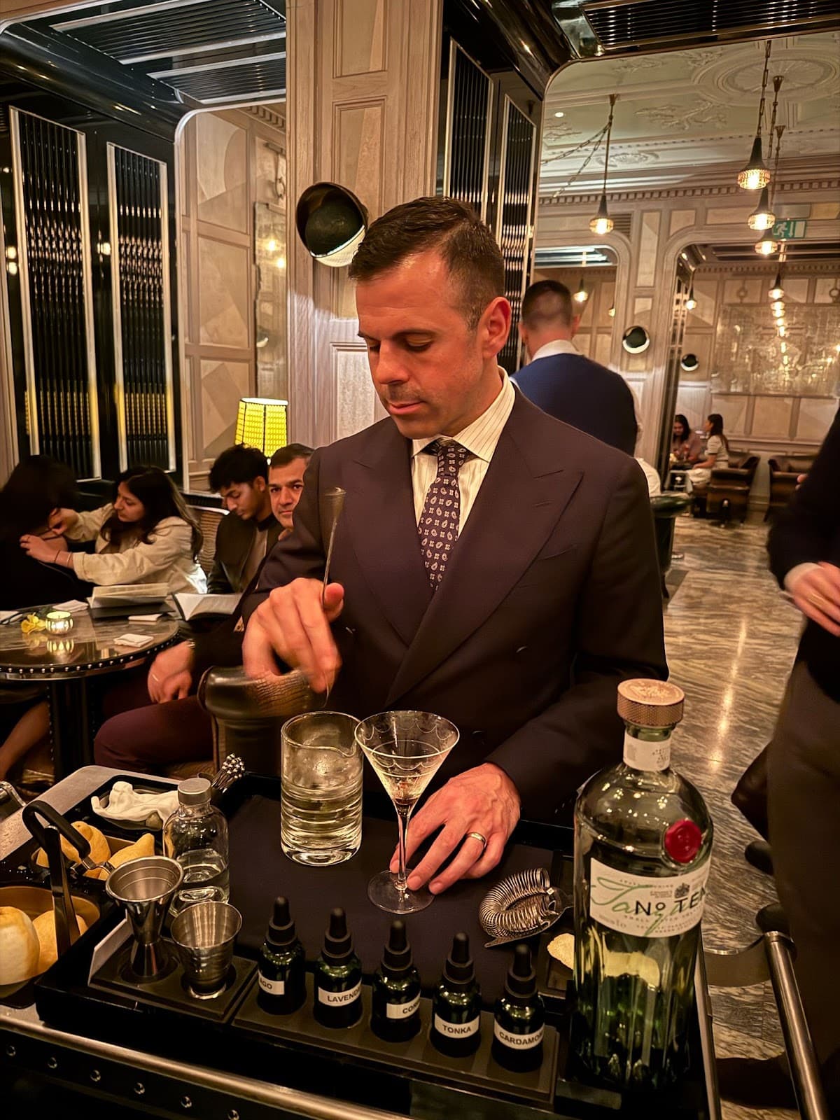 Bartender preparing cocktails with bottles and ingredients on a tray in a stylish bar setting in London