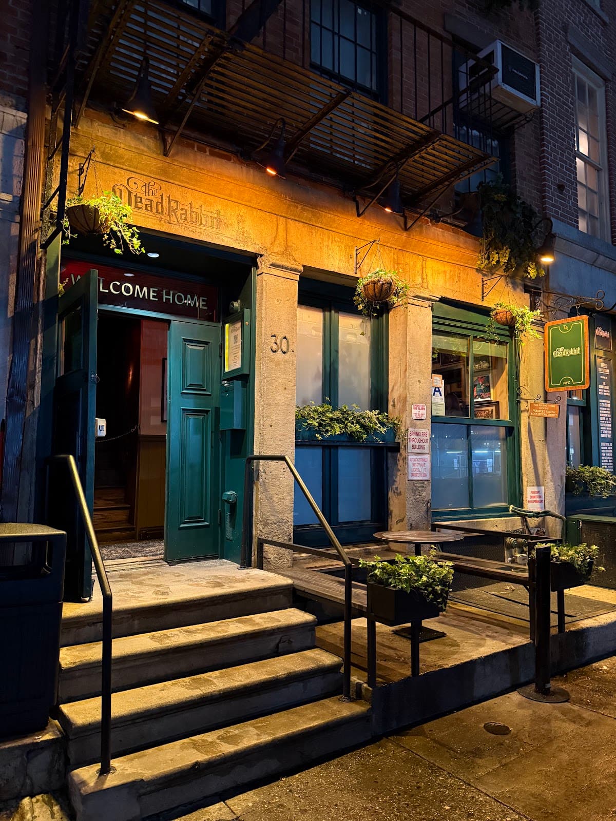 Evening exterior of The Dead Rabbit with illuminated entrance and steps in New York