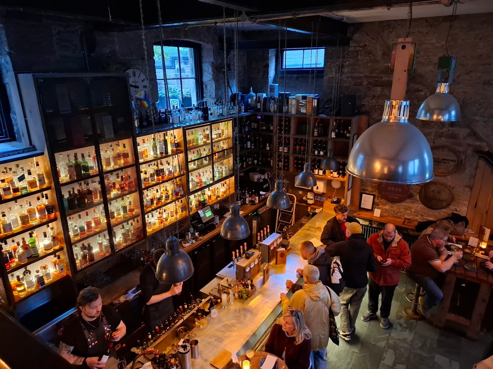 Overhead view of a bar with patrons, backlit shelves, and industrial lighting