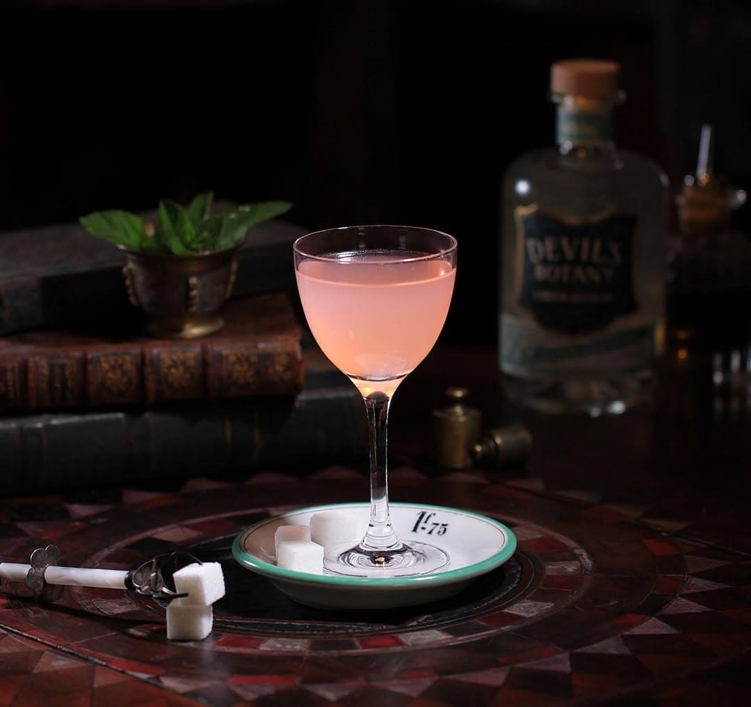 Pink cocktail on a table with sugar cubes and a bottle in the background in London