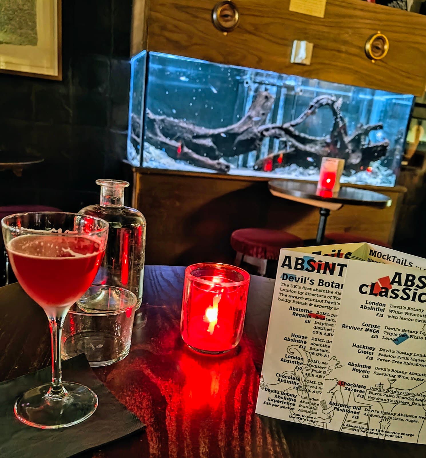 Cocktail on a table with a menu and candle in a dimly lit bar in London