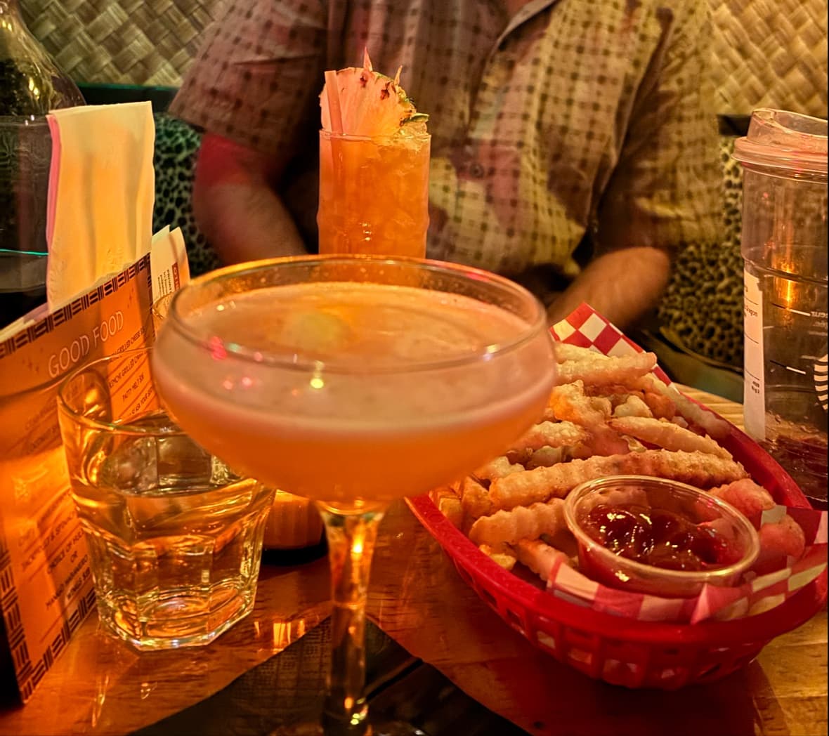 Two cocktails on a table with a basket of fries in a dimly lit setting in Toronto