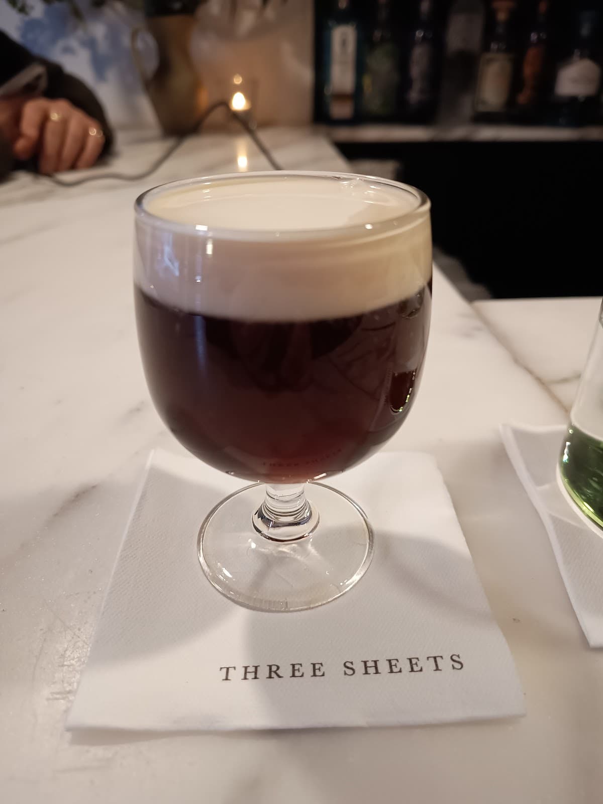 Cocktail on a napkin with 'Three Sheets' logo on a bar counter in London