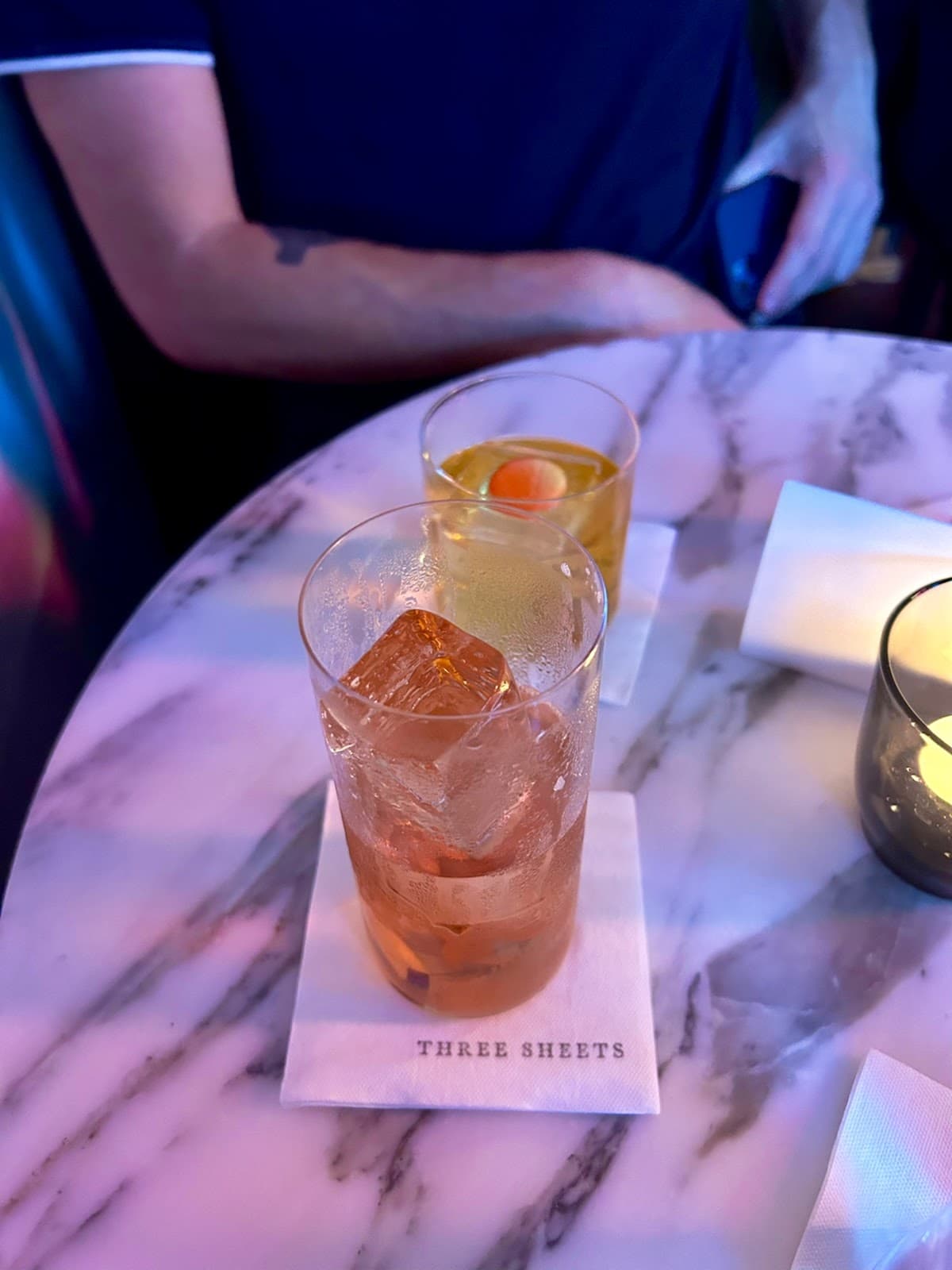 Two cocktails on a marble table with logo 'Three Sheets' on napkin in London