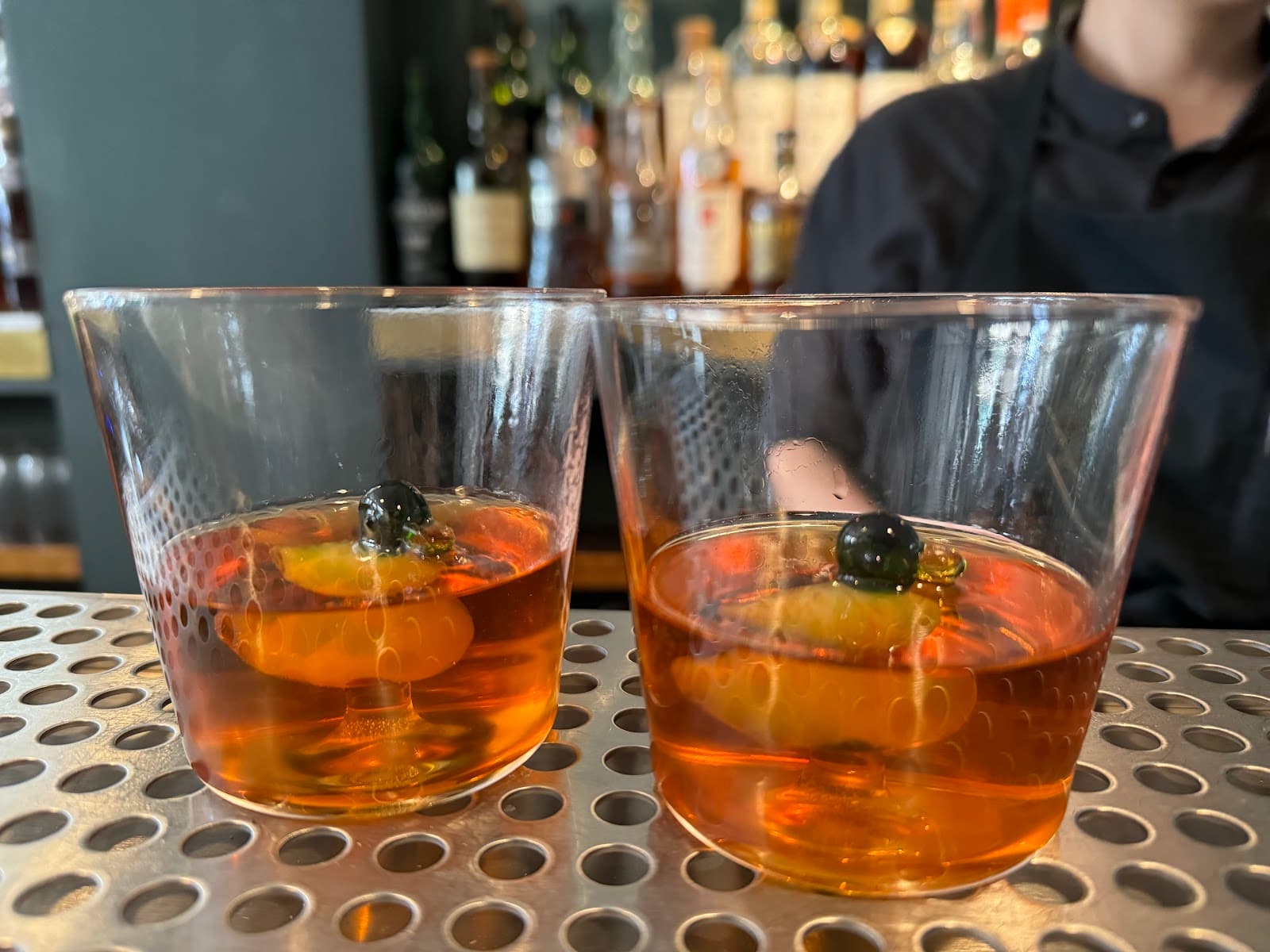 Two cocktails with garnishes on a perforated bar counter in London