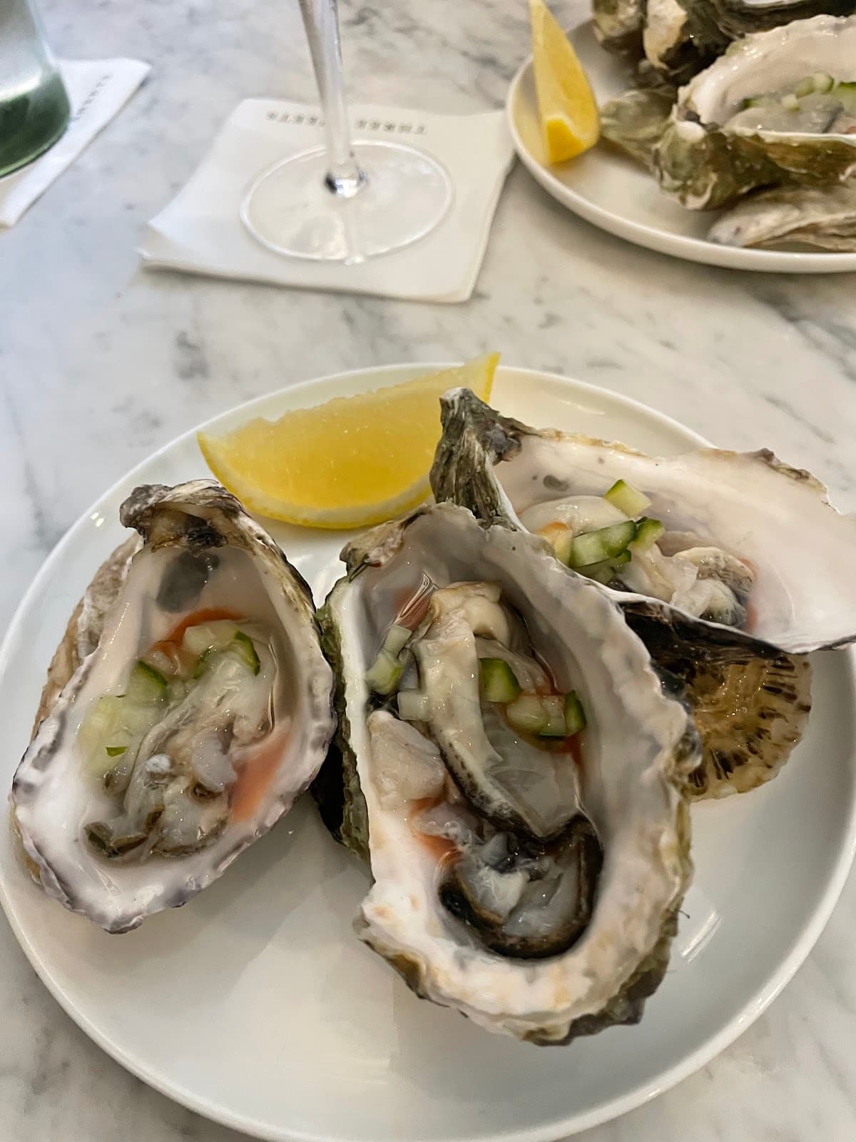 Plate of oysters with lemon slice on marble table at cocktail bar in London