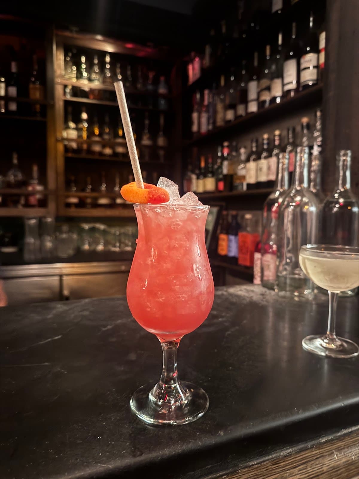 Vibrant red cocktail with ice and orange garnish at a dimly lit bar in San Francisco