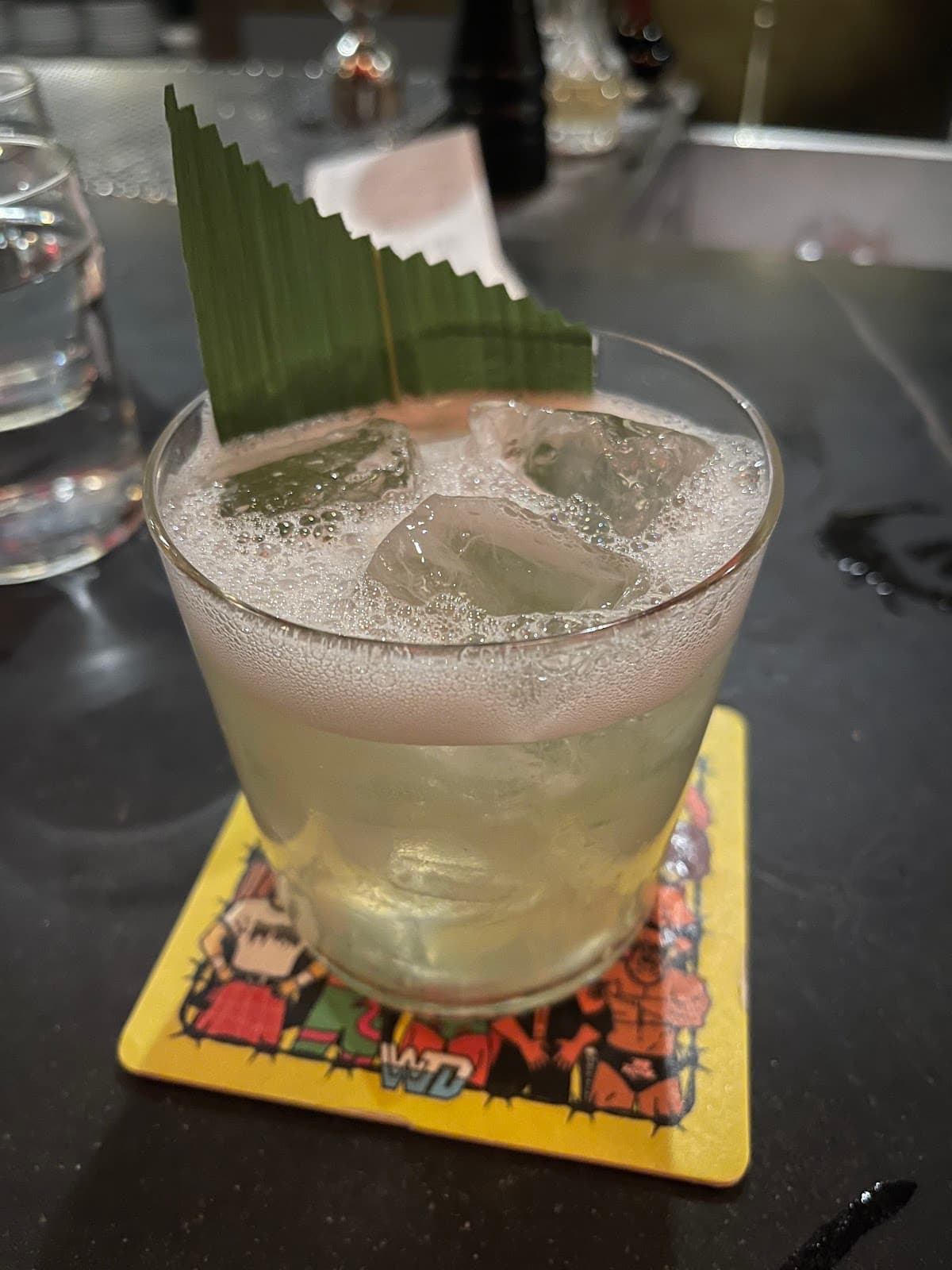 Close-up of a cocktail with a leaf garnish on a colorful coaster in San Francisco