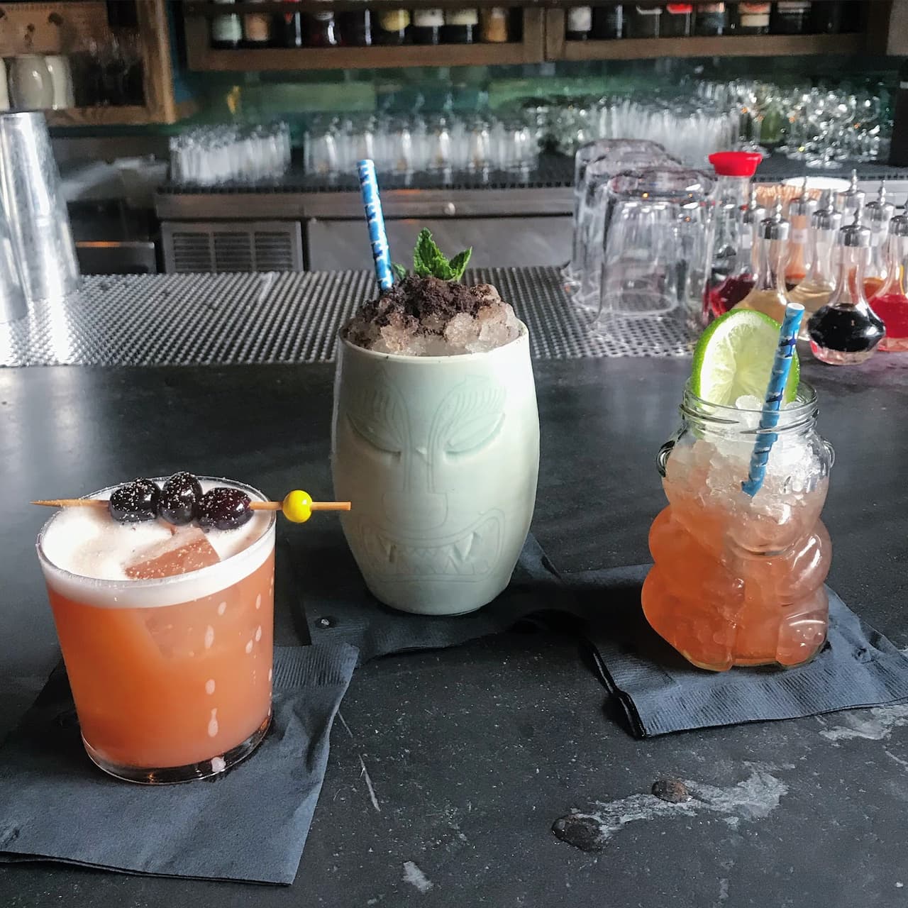 Three stylish cocktails on a bar counter with bottles and glasses in the background in San Francisco
