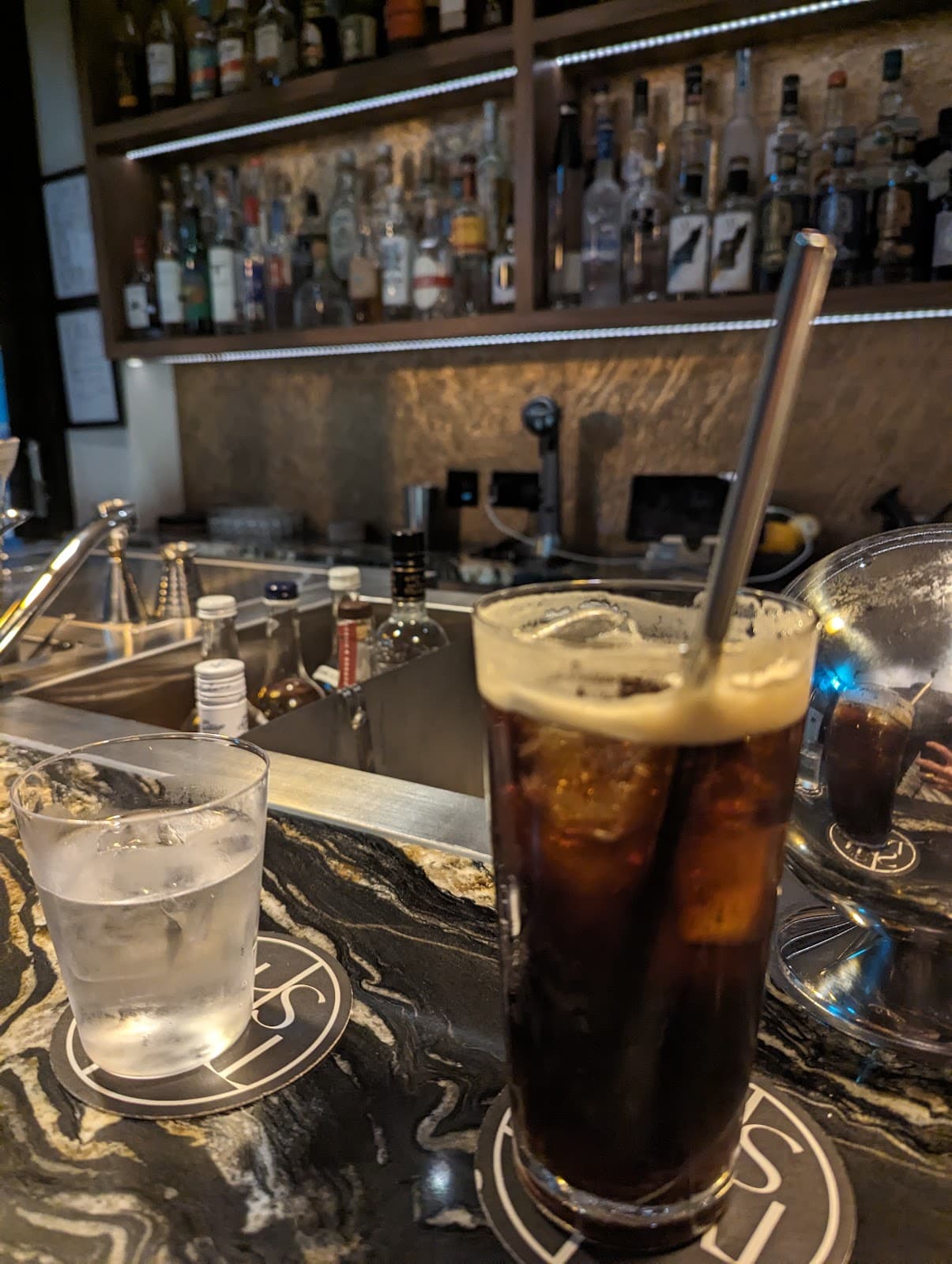 Close-up of bar counter with cocktails and backlit shelves in London