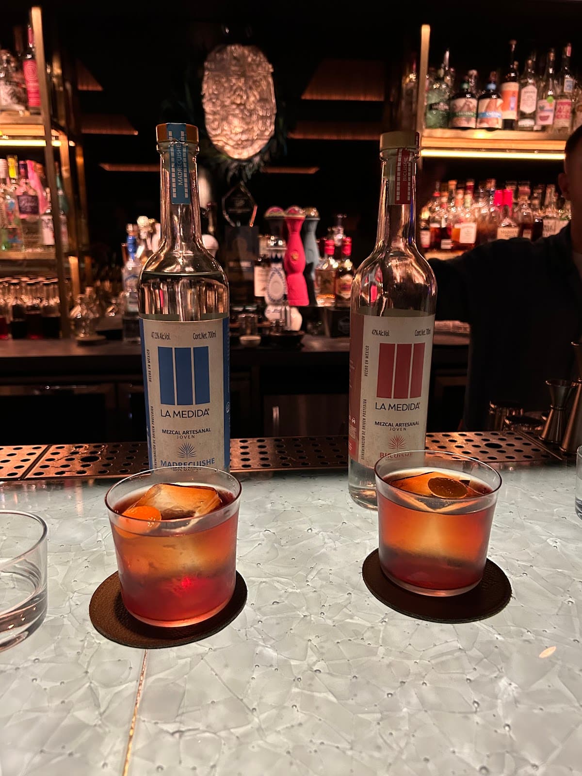 Bar counter with two La Medida mezcal bottles and cocktails in London